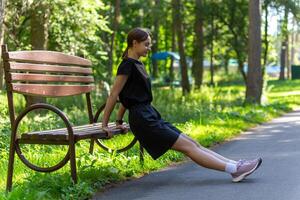 mooi jong sportief vrouw in zwart t-shirt, zwart shorts en roze trainers opwarming omhoog oefenen triceps foto