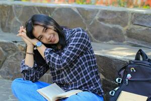 gelukkig jong Aziatisch vrouw college leerling met glimlachen gezicht genieten lezen een boek voor tentamen in de park foto