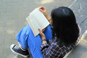 gelukkig bedachtzaam jong Aziatisch vrouw college leerling lezing een boek in de park, onderwijs concept foto