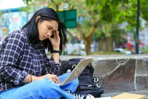 uitgeput en benadrukt Aziatisch vrouw leerling werken gebruik makend van laptop en studie met tekst boeken in buitenshuis foto