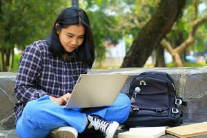 jong glimlachen Aziatisch vrouw gebruik makend van laptop en schrijven notitieboekje, vrolijk Aziatisch leerling aan het kijken webinar en aan het studeren van e Cursus foto