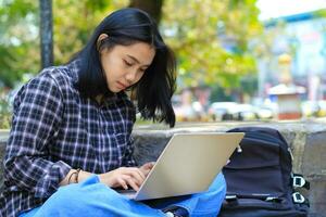 gelukkig jong Aziatisch vrouw gefocust gebruik makend van laptop werken van een afstand en browsen in sociaal media in comfortabel buitenshuis ruimte foto