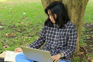 jong glimlachen Aziatisch vrouw gebruik makend van laptop en schrijven notitieboekje, vrolijk Aziatisch leerling aan het kijken webinar en aan het studeren van e Cursus foto