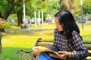 glimlachen Aziatisch mooi jong vrouw genieten schrijven naar Doen lijst en idee in notitieboekje in buitenshuis stad park foto