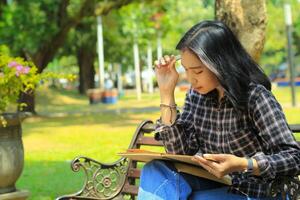 verwarrend Aziatisch jong vrouw denken een idee en schrijven in notitieboekje met een pen in natuur buitenshuis Oppervlakte foto