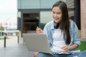 mooi Aziatisch vrouw vrouw leerling opgewonden controle taal test resultaten Aan laptop. glimlach meisje gelukkig studie online. boek in college campus. portret vrouw Aan Internationale Azië Universiteit foto