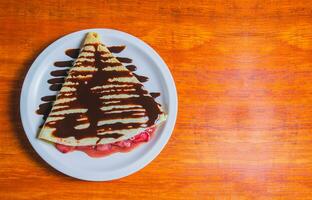 crêpe met chocola room en aardbei Aan houten tafel. zoet aardbei crêpe met chocola room Aan houten tafel foto