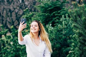 een mooie jonge vrouw die lacht en selfie maakt in een park foto