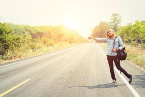 jonge hipster vrouw liftend op plattelandsweg wacht op de auto foto