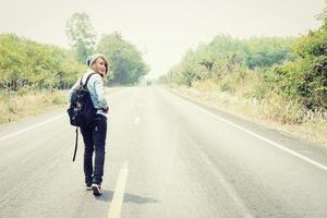 jonge vrouw liftend met rugzak zittend op de weg