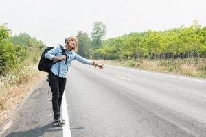 jonge hipster vrouw liftend op plattelandsweg wacht op de auto