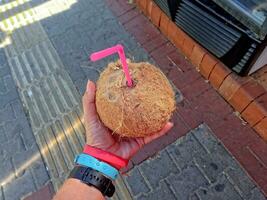 rijp kokosnoot in hand- met een plastic rietje gedurende een maaltijd foto