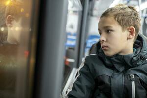 tiener- jongen in jasje op reis door bus in avond stad foto