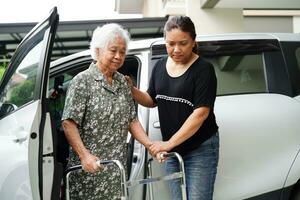 verzorger helpt aziatische bejaarde vrouw met een handicap om in haar auto te stappen, medisch concept. foto