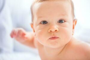 portret van schattig kleuter jongen aan het liegen Aan bed. pasgeboren kind in slaapkamer. baby leugens Aan zijn buik en verhoogt de hoofd foto