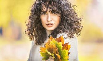 herfst portret van jong vrouw met gekruld haar- en boeket van esdoorn- bladeren foto