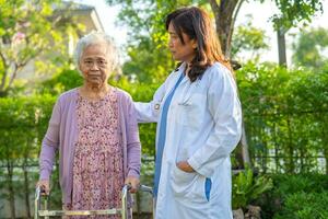 dokter verzorger helpen en zorg Aziatisch senior vrouw geduldig wandelen in park Bij ziekenhuis. foto