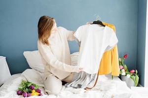 jonge vrouw die kleren organiseert die thuis op het bed zitten foto
