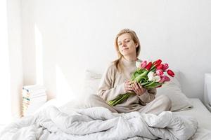 vrouw zittend op het bed in pyjama met tulpenbloemen foto