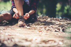 vrouw wandelaar stopt om haar schoen te binden op een zomer wandelpad in het bos. foto