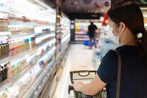 jonge vrouw die masker draagt dat voedsel in supermarkt winkelt
