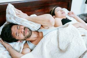 vrouw snurken in slaapkamer en man aan het bedekken zijn oren. man lijden van de snurken van zijn slapen vrouw. slaap apneu concept foto