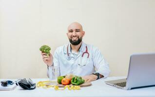 portret van glimlachen voedingsdeskundige Holding een broccoli. glimlachen voedingsdeskundige dokter Bij zijn bureau Holding een broccoli foto