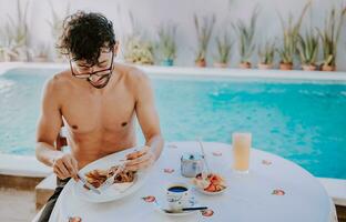 jong Mens Aan vakantie in hotel hebben ontbijt in de buurt zwemmen zwembad. ontbijt in de buurt de zwemmen zwembad. persoon hebben ontbijt in de hotel met zwembad in de achtergrond foto