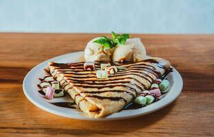 dichtbij omhoog van zoet crêpe met ijs room Aan houten tafel. chocola crêpe met ijs room Aan houten achtergrond foto