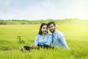 portret van een paar in liefde zittend Aan de gras in de veld, romantisch paar zittend Aan de gras op zoek Bij de camera, twee geliefden zittend Aan de gras op zoek Bij de camera foto