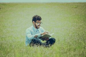 jong Mens Aan de gras lezing een boek, een persoon zittend Aan de gras lezing een boek, concept van mensen lezing buiten foto