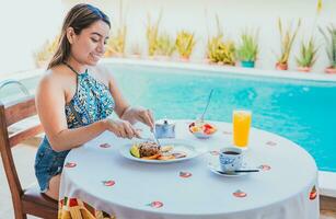 vrouw Aan vakantie hebben ontbijt in de buurt zwemmen zwembad. ontbijt concept in de buurt zwemmen zwembad, glimlachen meisje hebben ontbijt in de buurt de zwemmen zwembad foto