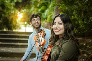 twee jong violisten zittend buitenshuis op zoek Bij de camera. portret van twee jong altviolisten zittend buiten. Mens en vrouw violist zittend Aan de trap. concept van twee jong violisten foto