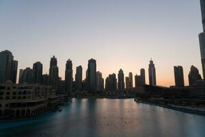 Dubai het zingen fonteinen Bij nacht meer visie tussen wolkenkrabbers. stad horizon in schemer modern architectuur in uae hoofdstad binnenstad. foto