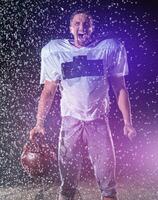 Amerikaans Amerikaans voetbal veld- eenzaam atleet krijger staand Aan een veld- houdt zijn helm en klaar naar Speel. speler voorbereidingen treffen naar rennen, aanval en partituur touchdown. regenachtig nacht met dramatisch mist, blauw licht foto