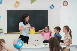 elementair school- wetenschap klas enthousiast leraar legt uit chemie naar verschillend groep van kinderen, weinig jongen mengsels Chemicaliën in bekers. kinderen leren met interesseren foto