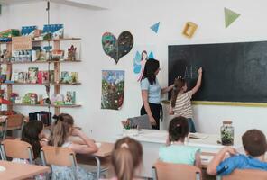 elementair school. de vrouw leraar helpen de kind leerling terwijl schrijven de antwoord Aan de schoolbord. foto