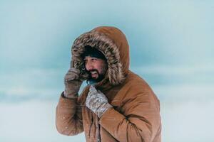 hoofdschot foto van een Mens in een verkoudheid besneeuwd Oppervlakte vervelend een dik bruin winter jasje en handschoenen. leven in verkoudheid Regio's van de land.
