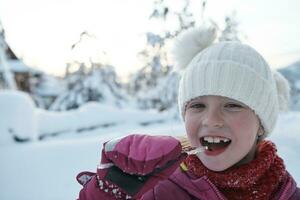 schattig weinig meisje terwijl aan het eten ijskegel Aan mooi winter dag foto