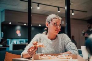 een modern blond aan het eten pizza in haar kantoor Aan een breken van werk foto