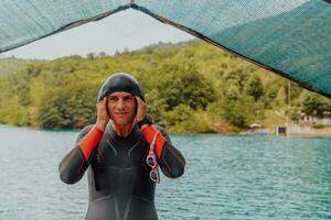 atleet zetten Aan een zwemmen pak en voorbereidingen treffen voor triatlon zwemmen en opleiding in de rivier- omringd door natuurlijk groen foto