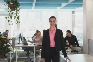 portret van jong glimlachen bedrijf vrouw in creatief Open ruimte coworking opstarten kantoor. geslaagd zakenvrouw in modern kantoor. team van collega's werken in achtergrond. foto