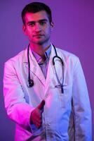 portret van een held in een wit jas. vrolijk glimlachen jong dokter met stethoscoop in medisch ziekenhuis staand Aan blauw en roze achtergrond. waarschuwing over de Gevaar van de coronavirus covid-19 foto