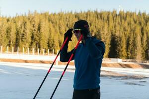 knap mannetje atleet met kruis land skis voorbereidingen treffen uitrusting voor opleiding in een besneeuwd Woud. controle smartwatch. gezond winter levensstijl. foto