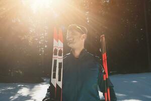portret knap mannetje atleet met kruis land skis in handen en stofbril, opleiding in besneeuwd Woud. gezond winter levensstijl concept. foto