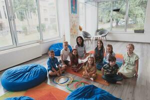 een gelukkig vrouw leraar zittend en spelen hand- spellen met een groep van weinig schoolkinderen foto