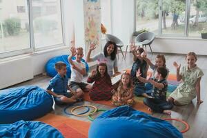 een gelukkig vrouw leraar zittend en spelen hand- spellen met een groep van weinig schoolkinderen foto