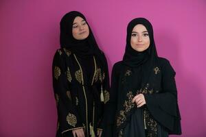 twee mooi moslim vrouw in modieus jurk met hijab geïsoleerd Aan modern roze achtergrond vertegenwoordigen concept van modern Islam en Ramadan kareem foto