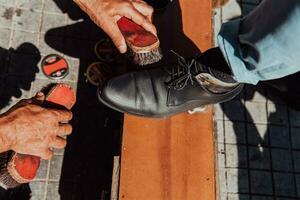 een oud Mens hand- polijsten en schilderij een zwart schoen Bij straat foto