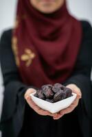 modern moslim vrouw Holding een bord vol van zoet datums Aan iftar tijd in Ramadan kareem Islamitisch gezond voedsel concept foto